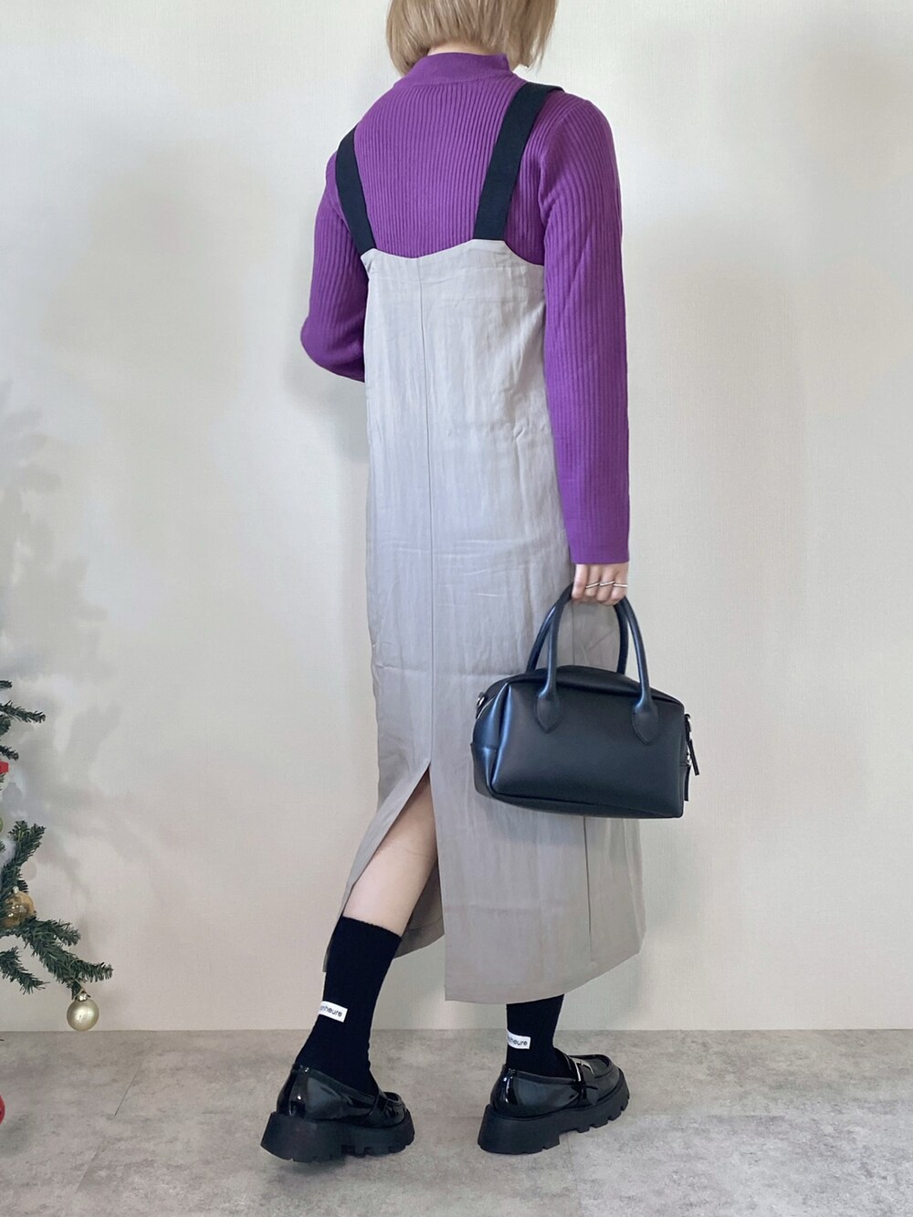 パープル系のニット/セーター、グレー系のジャンパースカート、ブラック系のバッグを着用したレディースの冬コーディネートの4枚目の写真