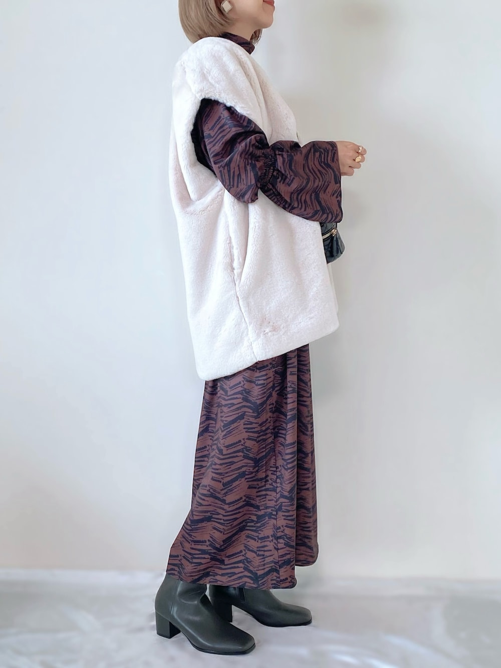 ブラウン系のワンピース、ブラック系のショルダーバッグ、ホワイト系のベストを着用したレディースの秋コーディネートの2枚目の写真