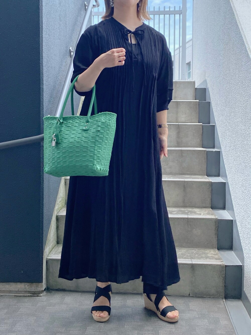 グリーン系のバッグ、ブラック系のサンダル、ブラック系のワンピースを着用したレディースの夏コーディネートの2枚目の写真
