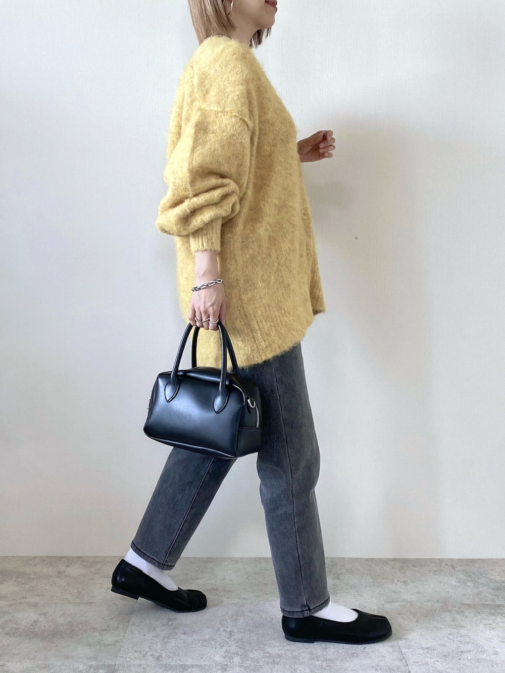 イエロー系のカーディガン/ボレロ、ブラック系のバッグ、グレー系のデニムパンツを着用したレディースの冬コーディネートの2枚目の写真