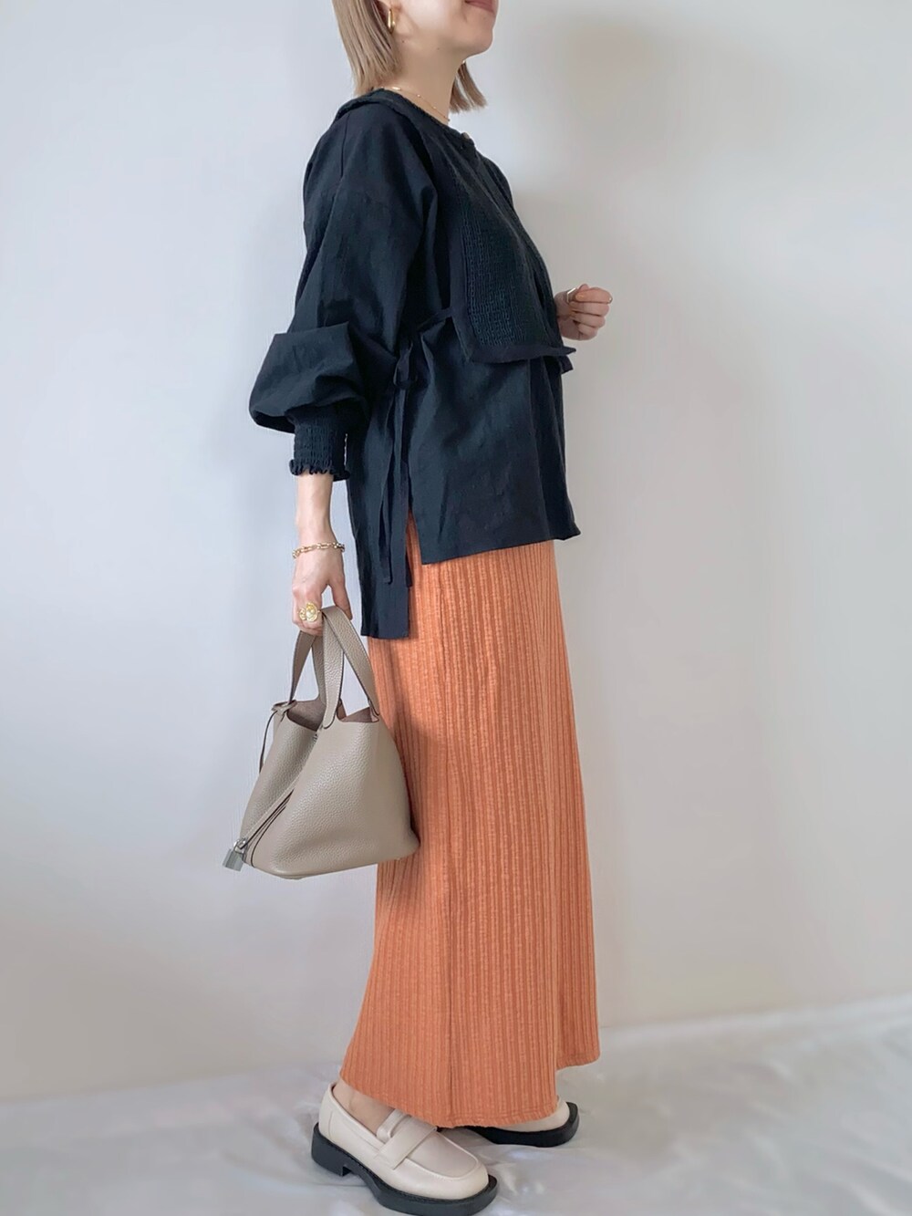 オレンジ系のスカート、ベージュ系のローファー、ブラック系のシャツ/ブラウスを着用したレディースの春コーディネートの2枚目の写真