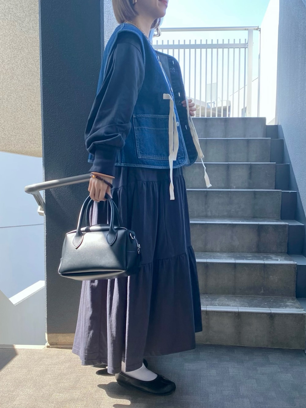 グレー系のワンピース、ブルー系のベスト、ブラック系のパンプスを着用したレディースの春コーディネートの2枚目の写真