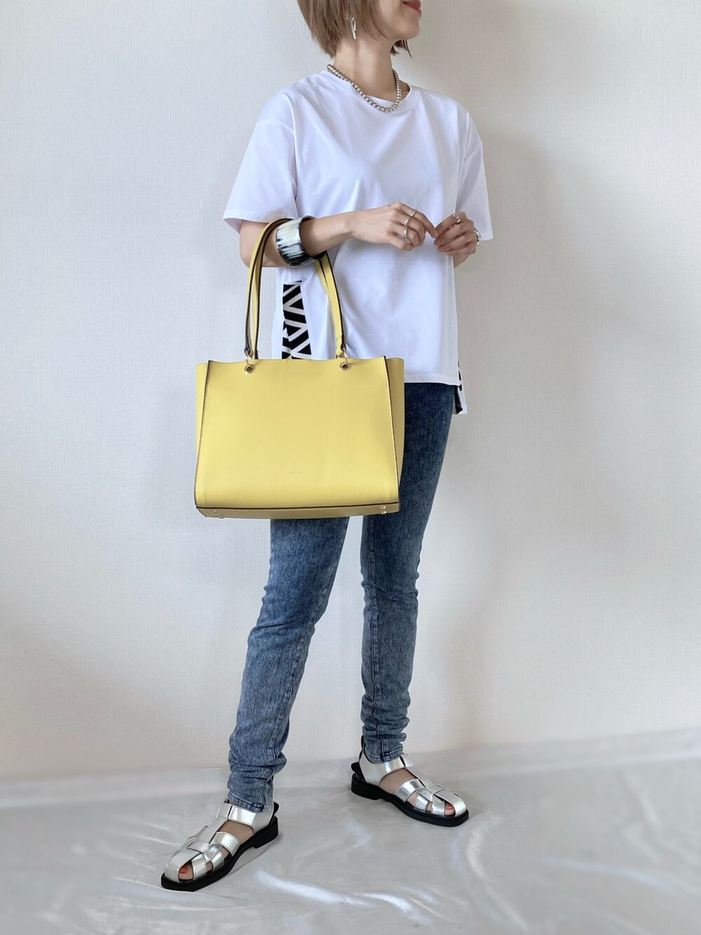 イエロー系のトートバッグ、ホワイト系のトップス、シルバー系のサンダルを着用したレディースの夏コーディネートの2枚目の写真