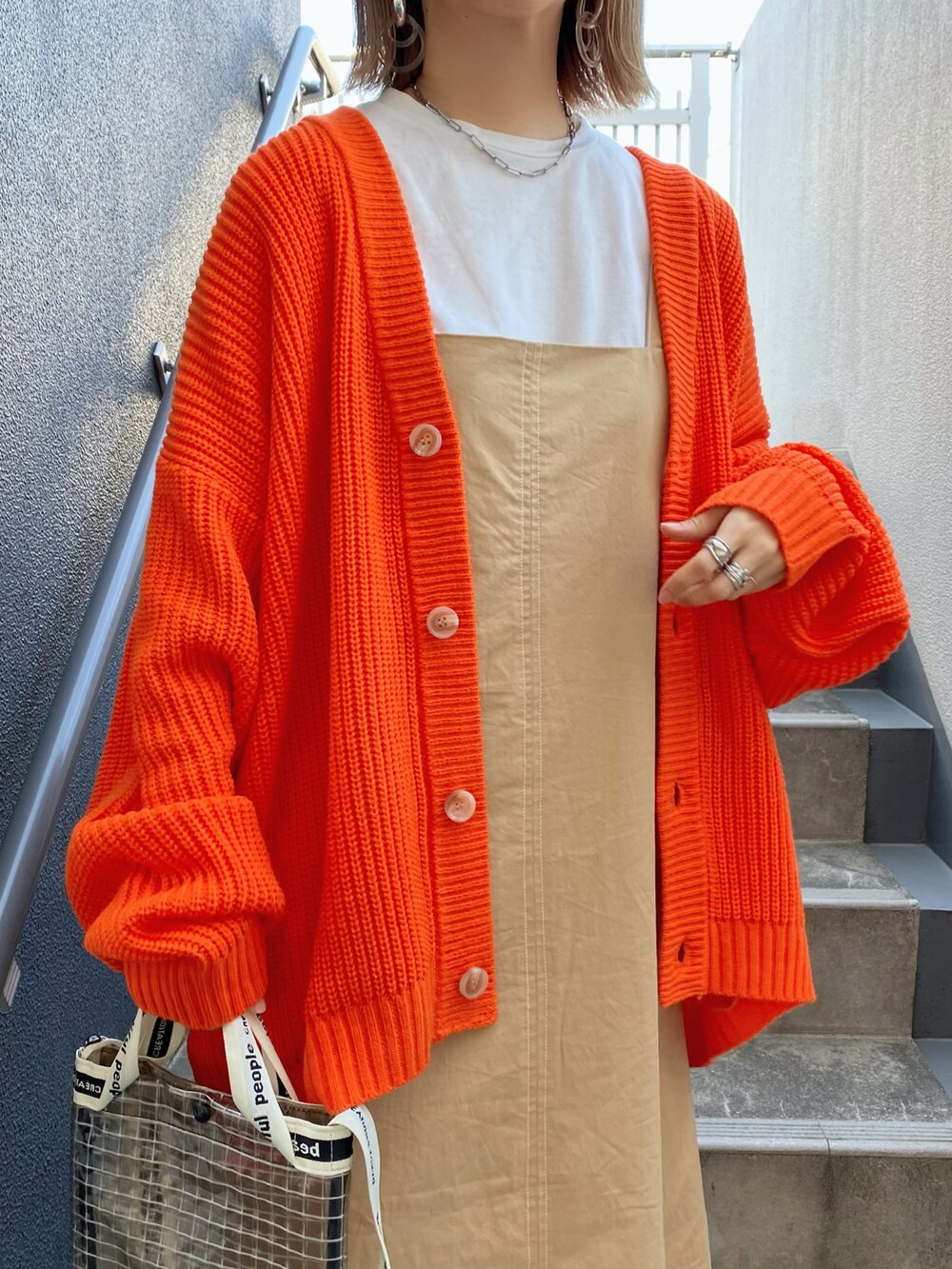 オレンジ系のカーディガン/ボレロ、ベージュ系のワンピース、ブラック系のショルダーバッグを着用したレディースの春コーディネートの4枚目の写真