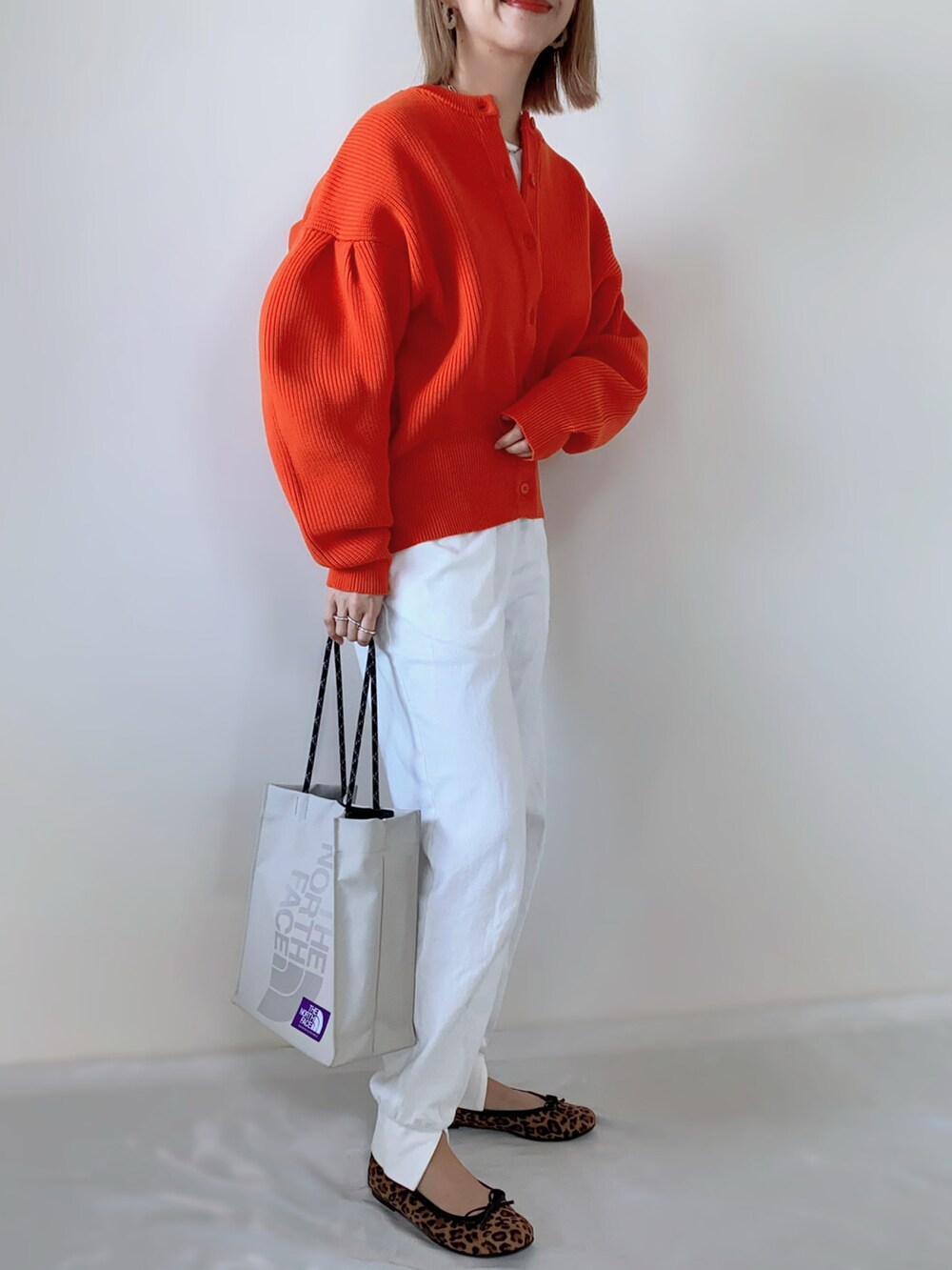 オレンジ系のカーディガン/ボレロ、ホワイト系のその他パンツ、ベージュ系のトートバッグを着用したレディースの春コーディネートの2枚目の写真