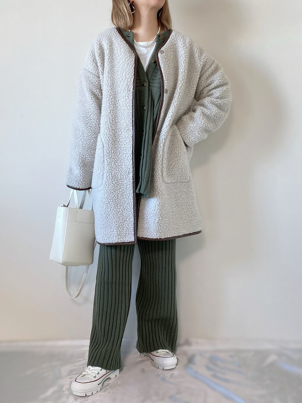 グリーン系のニット/セーター、ホワイト系のムートンコート、ホワイト系のバッグを着用したレディースの冬コーディネートの2枚目の写真