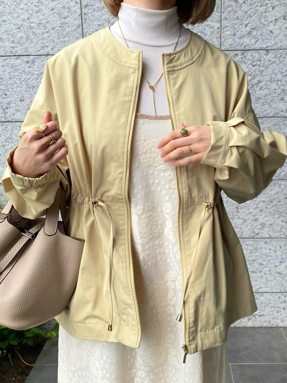 イエロー系のブルゾン、ホワイト系のワンピース、ブラウン系のパンプスを着用したレディースの春コーディネートの4枚目の写真