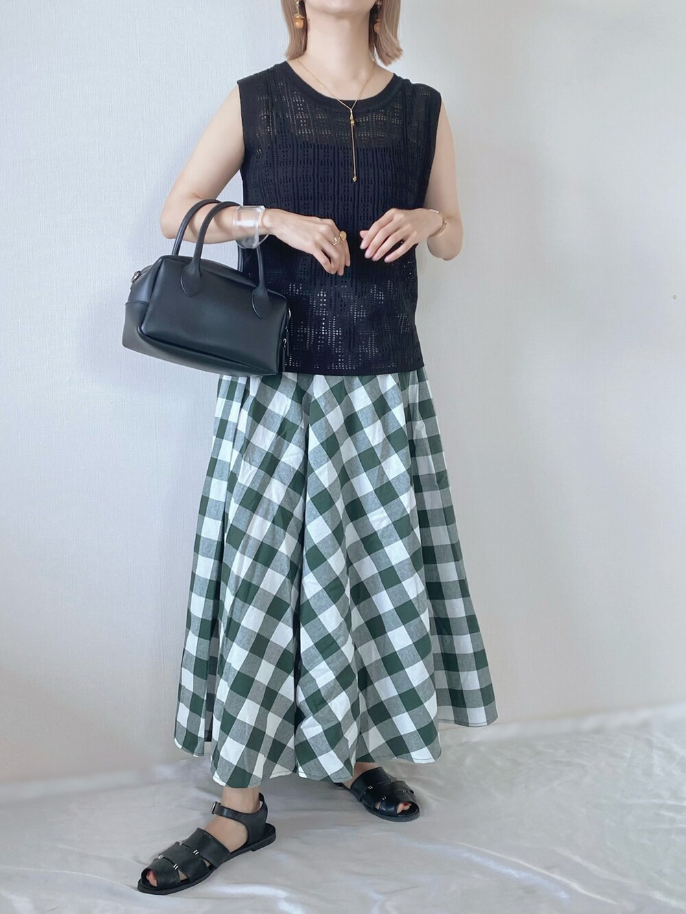 ブラック系のニット/セーター、ブラック系のバッグ、グリーン系のスカートを着用したレディースの春コーディネートの2枚目の写真