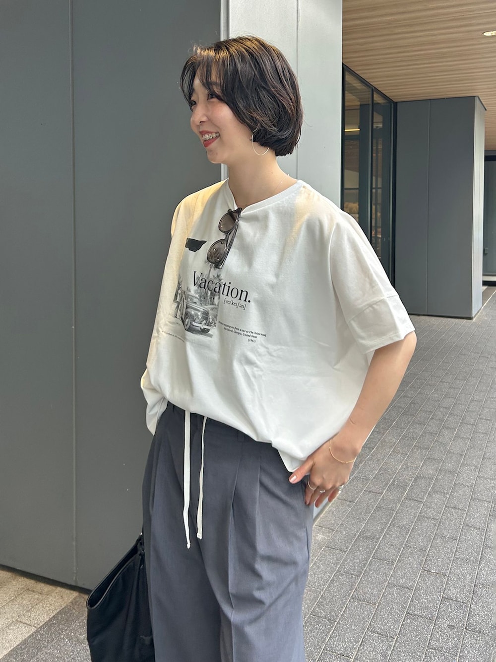 グレー系のスラックス、ブラック系のトートバッグ、ブラック系のサンダルを着用したレディースの夏コーディネートの5枚目の写真