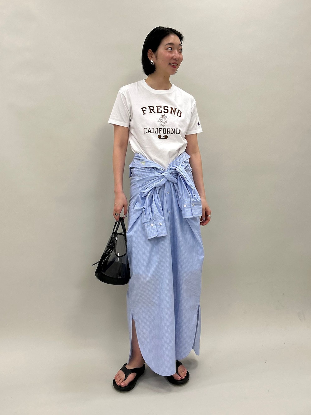 ブルー系のシャツワンピース、ホワイト系のTシャツ/カットソー、ブラック系のハンドバッグを着用したレディースの春コーディネートの2枚目の写真