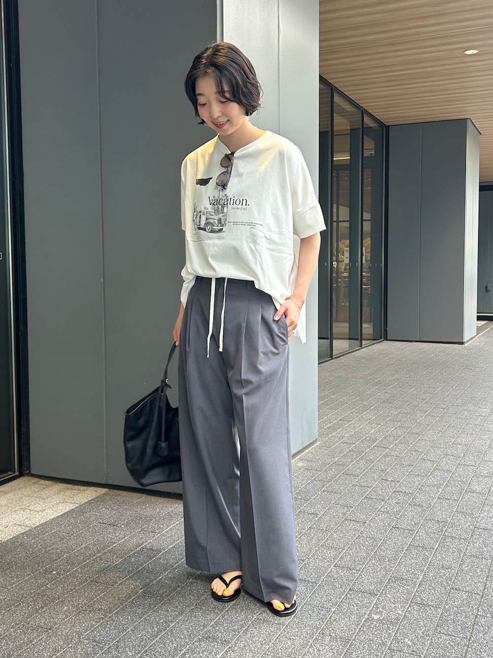 グレー系のスラックス、ホワイト系のTシャツ/カットソー、ブラック系のトートバッグを着用したレディースの夏コーディネートの2枚目の写真