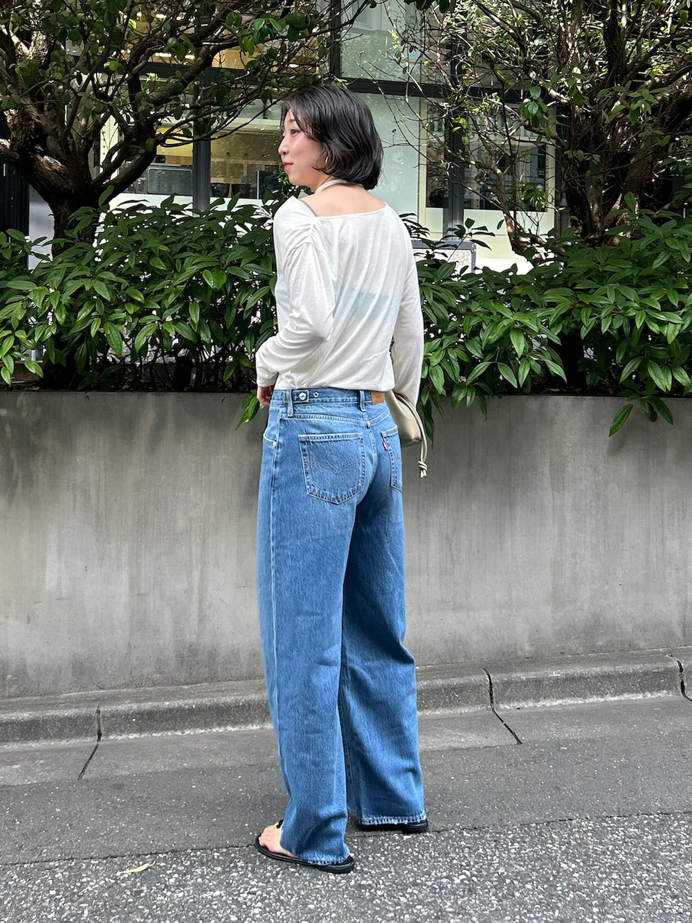 ブルー系のデニムパンツ、ホワイト系のTシャツ/カットソー、ベージュ系のクラッチバッグを着用したレディースの夏コーディネートの3枚目の写真