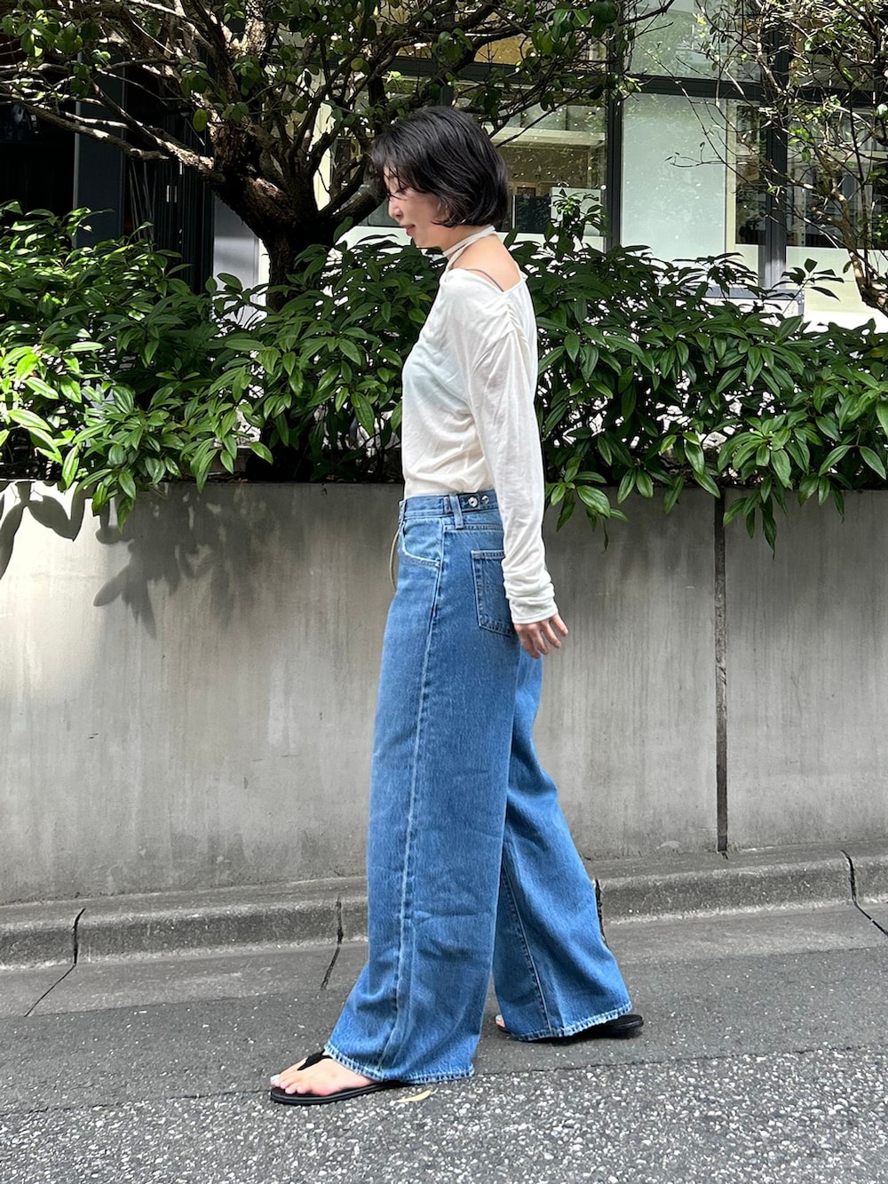 ブルー系のデニムパンツ、ホワイト系のTシャツ/カットソー、ベージュ系のクラッチバッグを着用したレディースの夏コーディネートの2枚目の写真