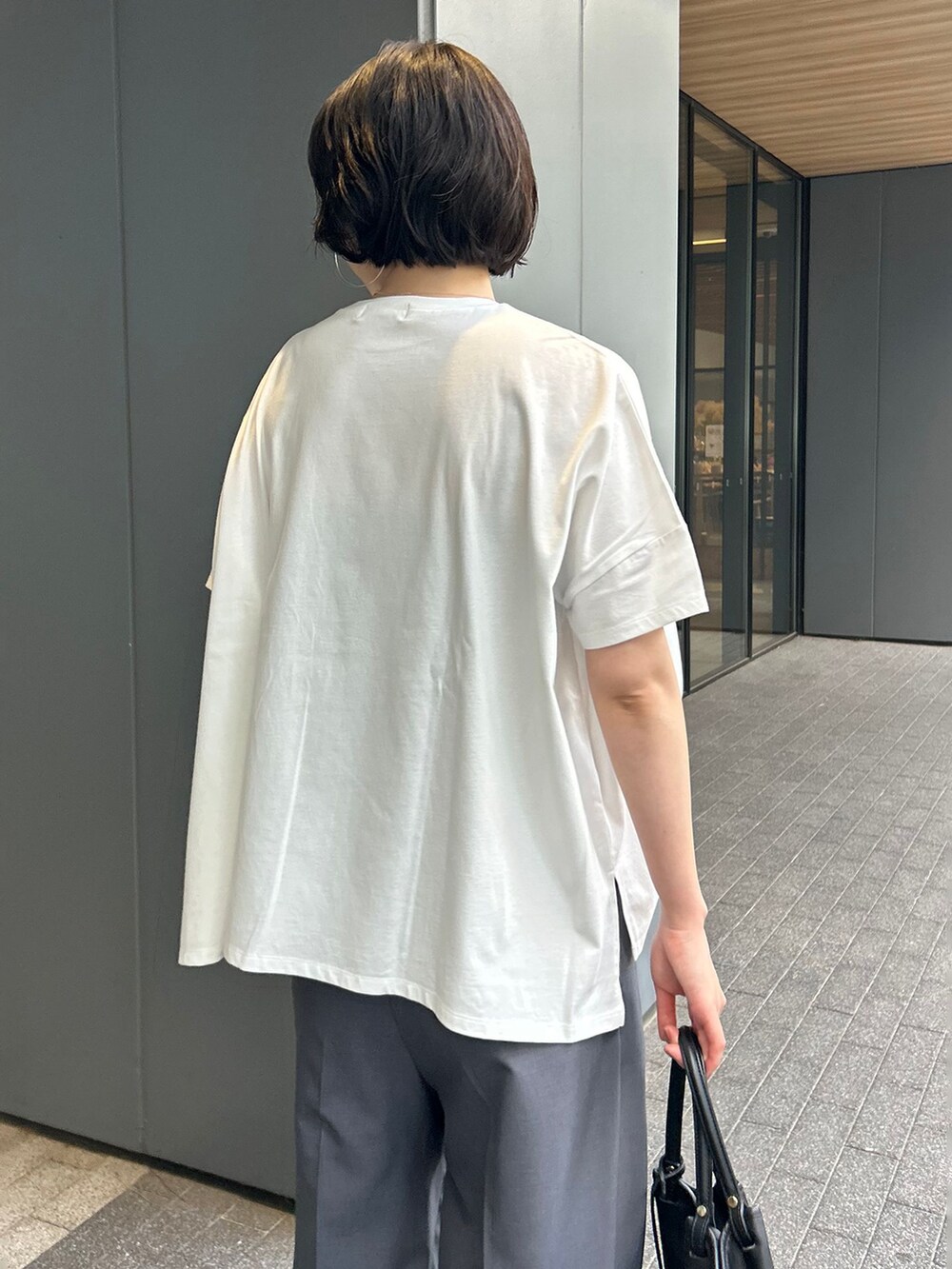 グレー系のスラックス、ホワイト系のTシャツ/カットソー、ブラック系のトートバッグを着用したレディースの夏コーディネートの7枚目の写真