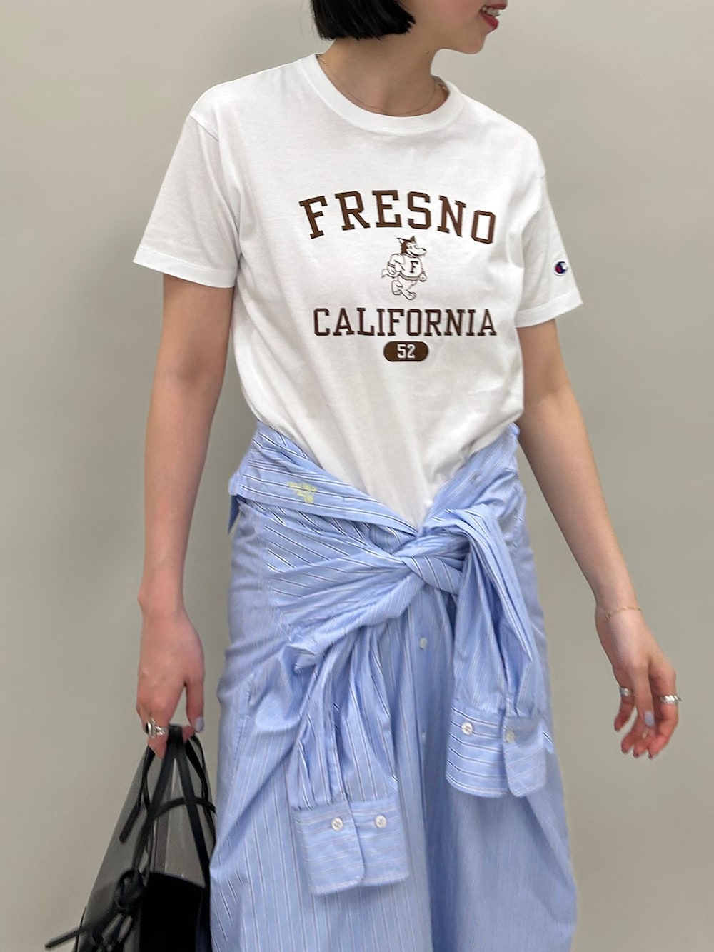 ブルー系のシャツワンピース、ホワイト系のTシャツ/カットソー、ブラック系のハンドバッグを着用したレディースの春コーディネートの4枚目の写真