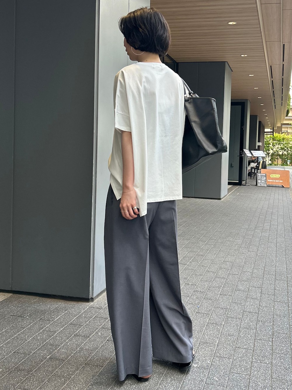 グレー系のスラックス、ホワイト系のTシャツ/カットソー、ブラック系のトートバッグを着用したレディースの夏コーディネートの3枚目の写真