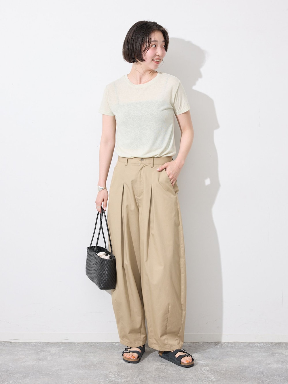 ベージュ系のチノパンツ、グリーン系のTシャツ/カットソー、ブラック系のかごバッグを着用したレディースの夏コーディネートの2枚目の写真