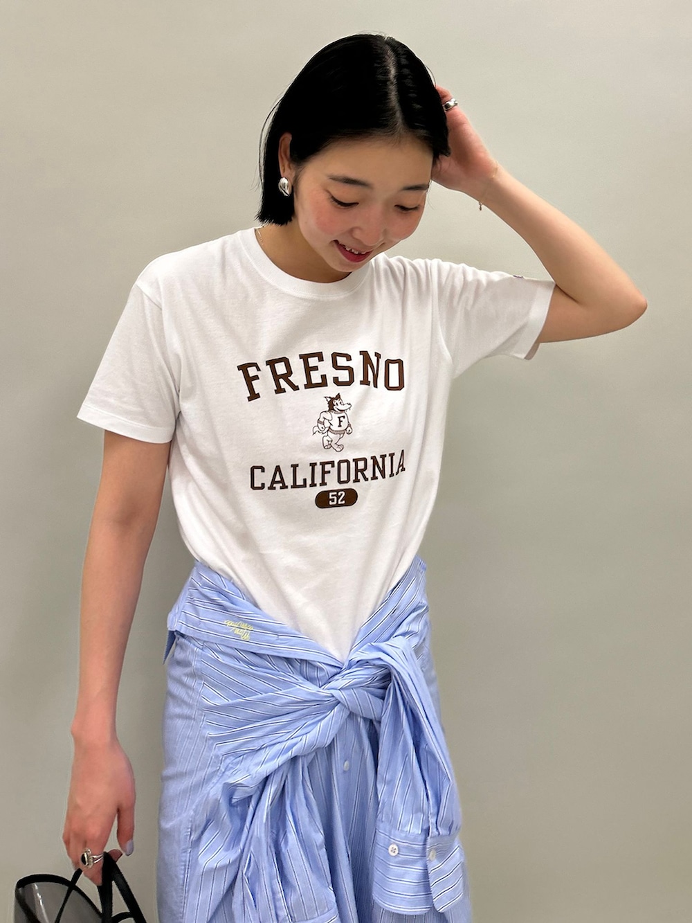 ブルー系のシャツワンピース、ホワイト系のTシャツ/カットソー、ブラック系のハンドバッグを着用したレディースの春コーディネートの5枚目の写真