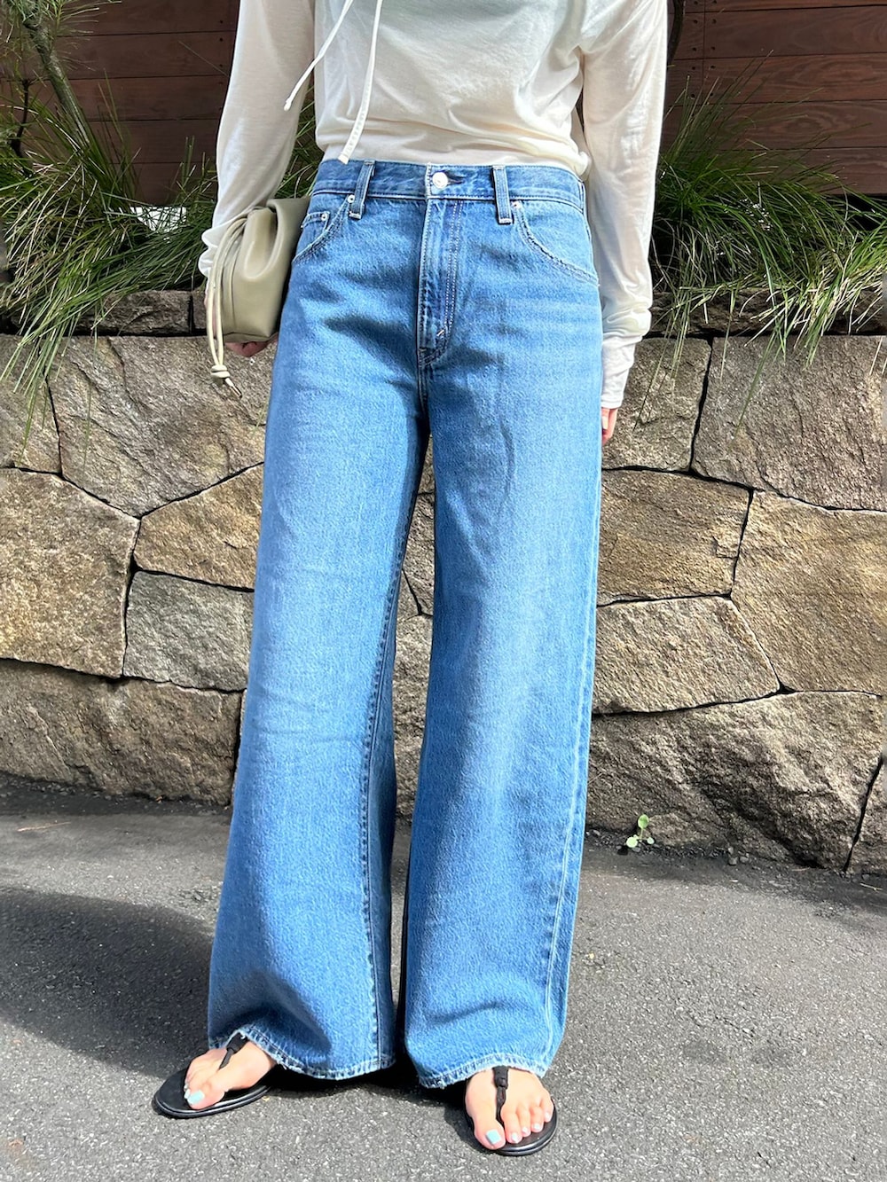 ブルー系のデニムパンツ、ホワイト系のTシャツ/カットソー、ベージュ系のクラッチバッグを着用したレディースの夏コーディネートの4枚目の写真