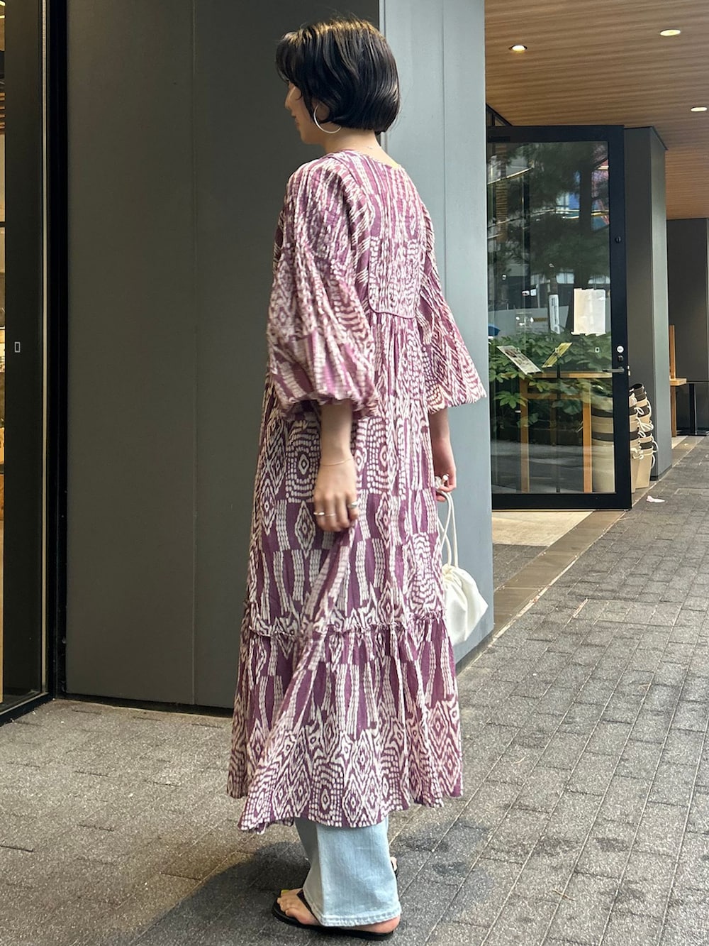 ブルー系のデニムパンツ、パープル系のワンピース、ホワイト系のクラッチバッグを着用したレディースの夏コーディネートの3枚目の写真