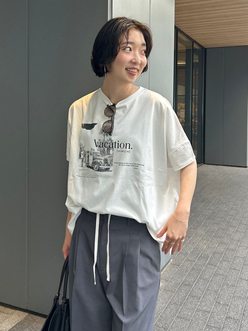 グレー系のスラックス、ホワイト系のTシャツ/カットソー、ブラック系のトートバッグを着用したレディースの夏コーディネートの4枚目の写真