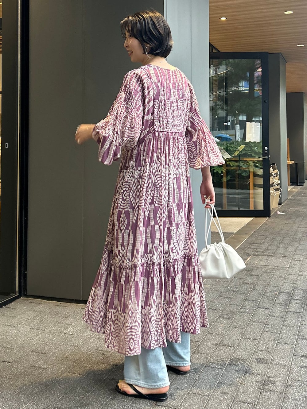 ブルー系のデニムパンツ、パープル系のワンピース、ホワイト系のクラッチバッグを着用したレディースの夏コーディネートの4枚目の写真