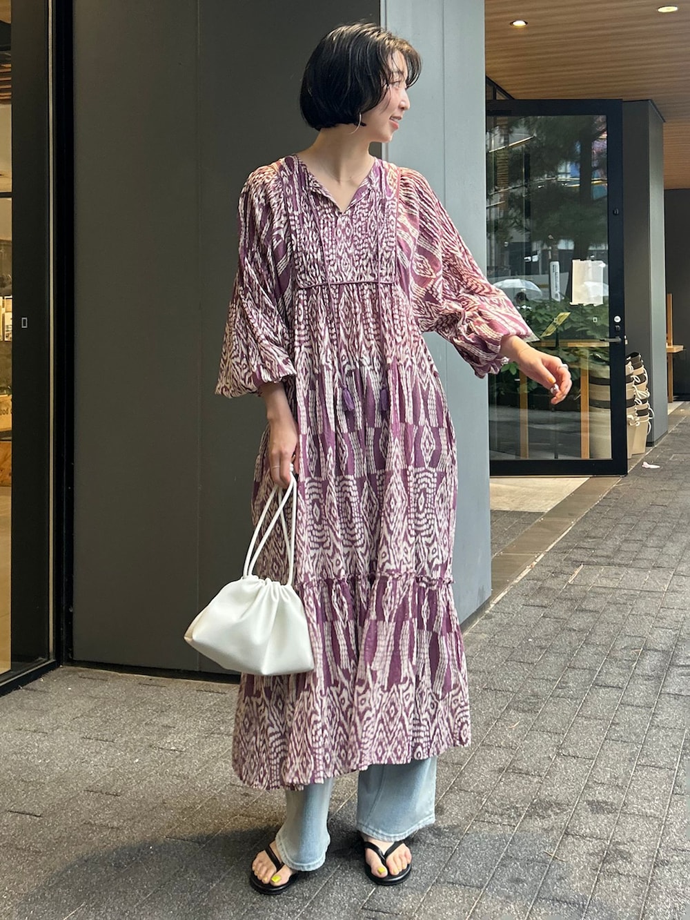 ブルー系のデニムパンツ、パープル系のワンピース、ホワイト系のクラッチバッグを着用したレディースの夏コーディネートの2枚目の写真