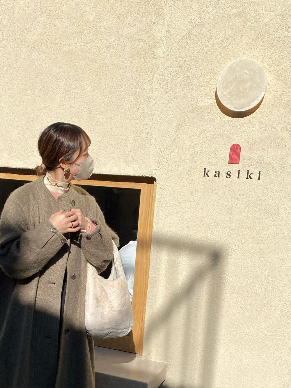 ブラウン系のブーツ、ブラウン系のノーカラーコート、ホワイト系のバッグを着用したレディースの春コーディネートの4枚目の写真