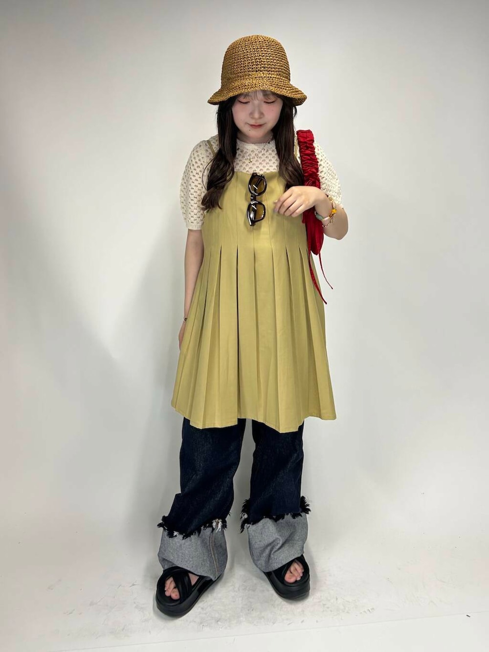 レッド系のハンドバッグ、ブルー系のデニムパンツ、ベージュ系のワンピースを着用したレディースの夏コーディネートの2枚目の写真