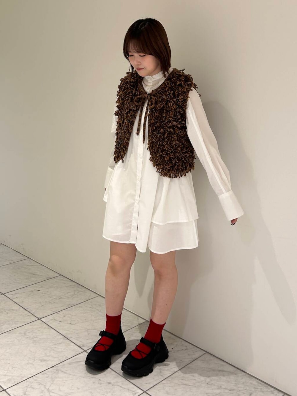 ブラック系のスニーカー、ブラウン系のベスト、ホワイト系のワンピースを着用したレディースの夏コーディネートの3枚目の写真