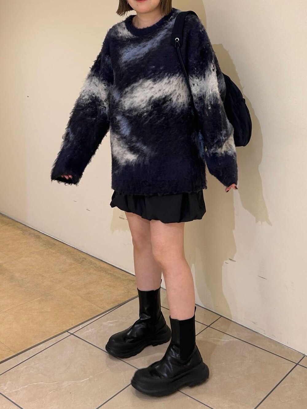 グレー系のスカート、ブラック系のブーツ、ブルー系のショルダーバッグを着用したレディースの秋コーディネートの2枚目の写真