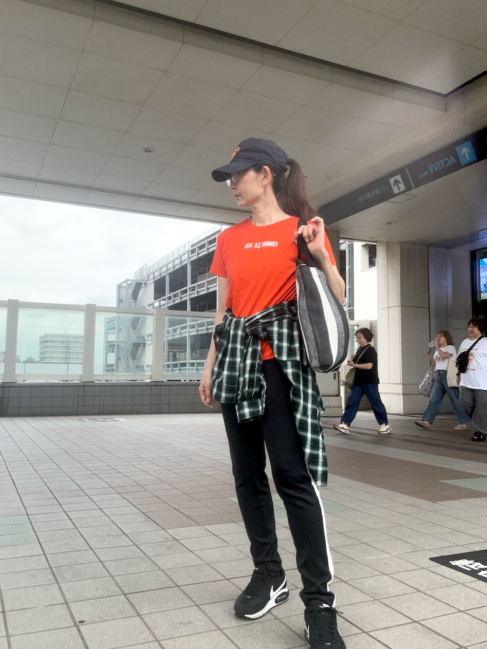 オレンジ系のTシャツ/カットソー、ブラック系のスニーカー、グリーン系のシャツ/ブラウスを着用したレディースの夏コーディネートの2枚目の写真