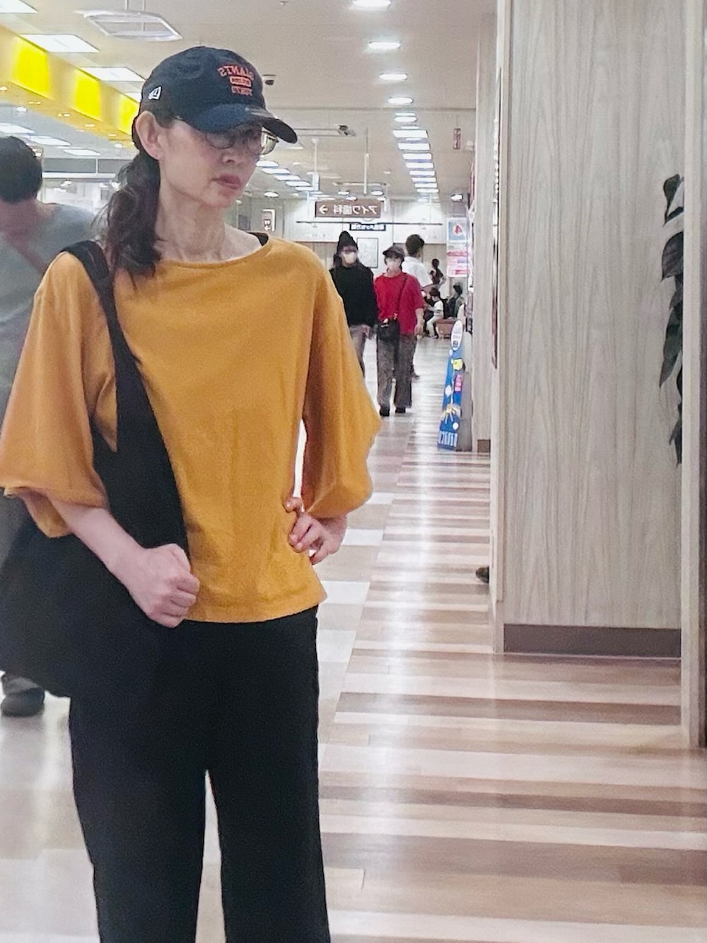 ブラック系のスラックス、オレンジ系のTシャツ/カットソー、ブラウン系のサンダルを着用したレディースの春コーディネートの2枚目の写真