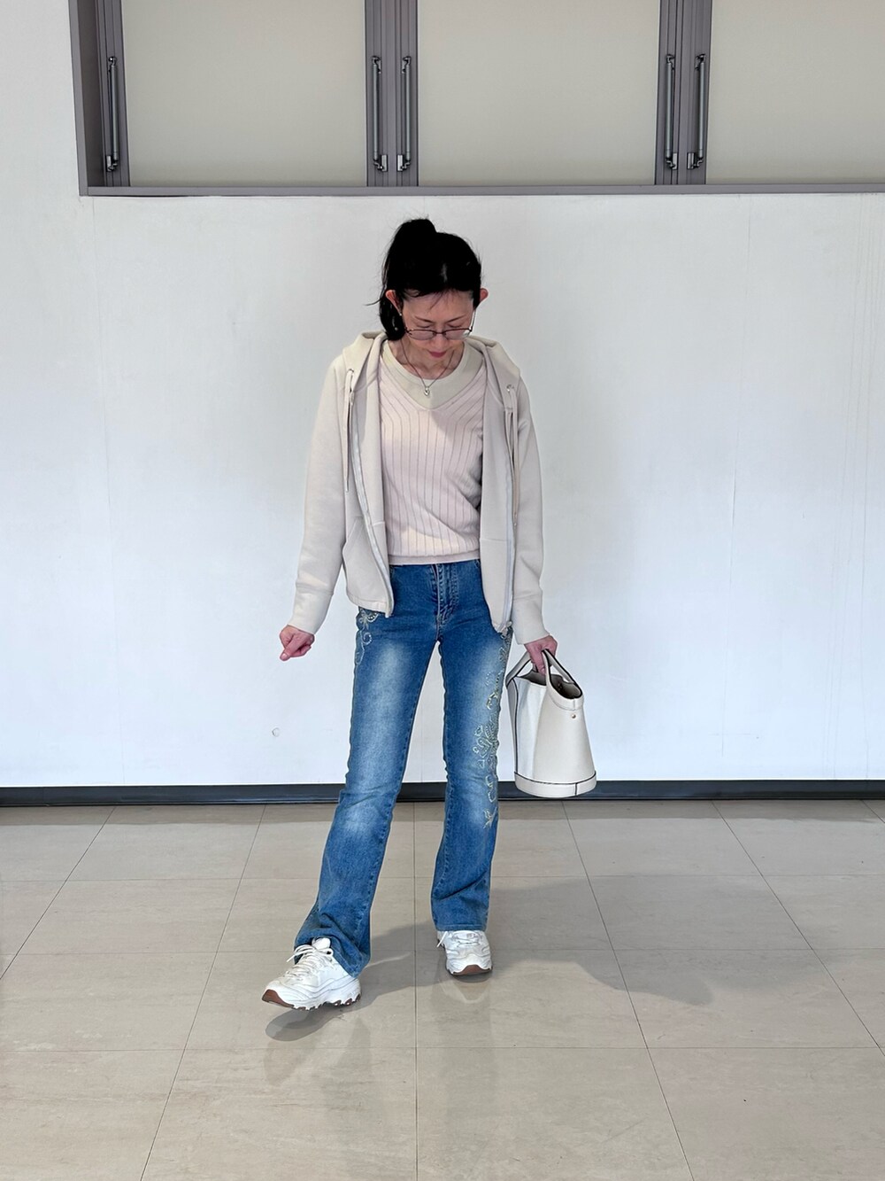 ベージュ系のニット/セーター、ベージュ系のハンドバッグ、ホワイト系のスニーカーを着用したレディースの春コーディネートの2枚目の写真