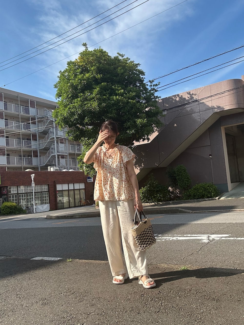 オレンジ系のシャツ/ブラウス、ホワイト系のスラックス、その他のかごバッグを着用したレディースの夏コーディネートの2枚目の写真