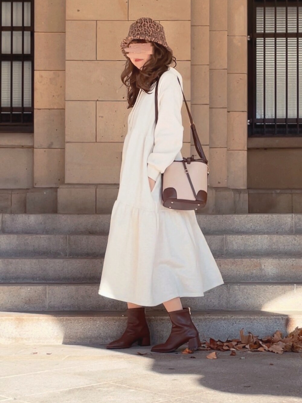ホワイト系のワンピース、ブラウン系のブーツ、ホワイト系のショルダーバッグを着用したレディースの冬コーディネートの2枚目の写真
