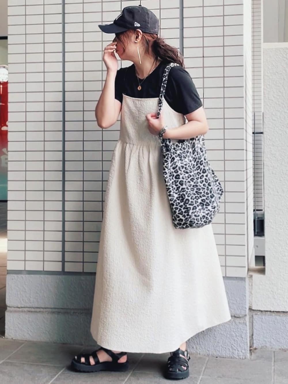 ホワイト系のワンピース、ブラック系のトートバッグ、ブルー系のキャップを着用したレディースの夏コーディネートの2枚目の写真