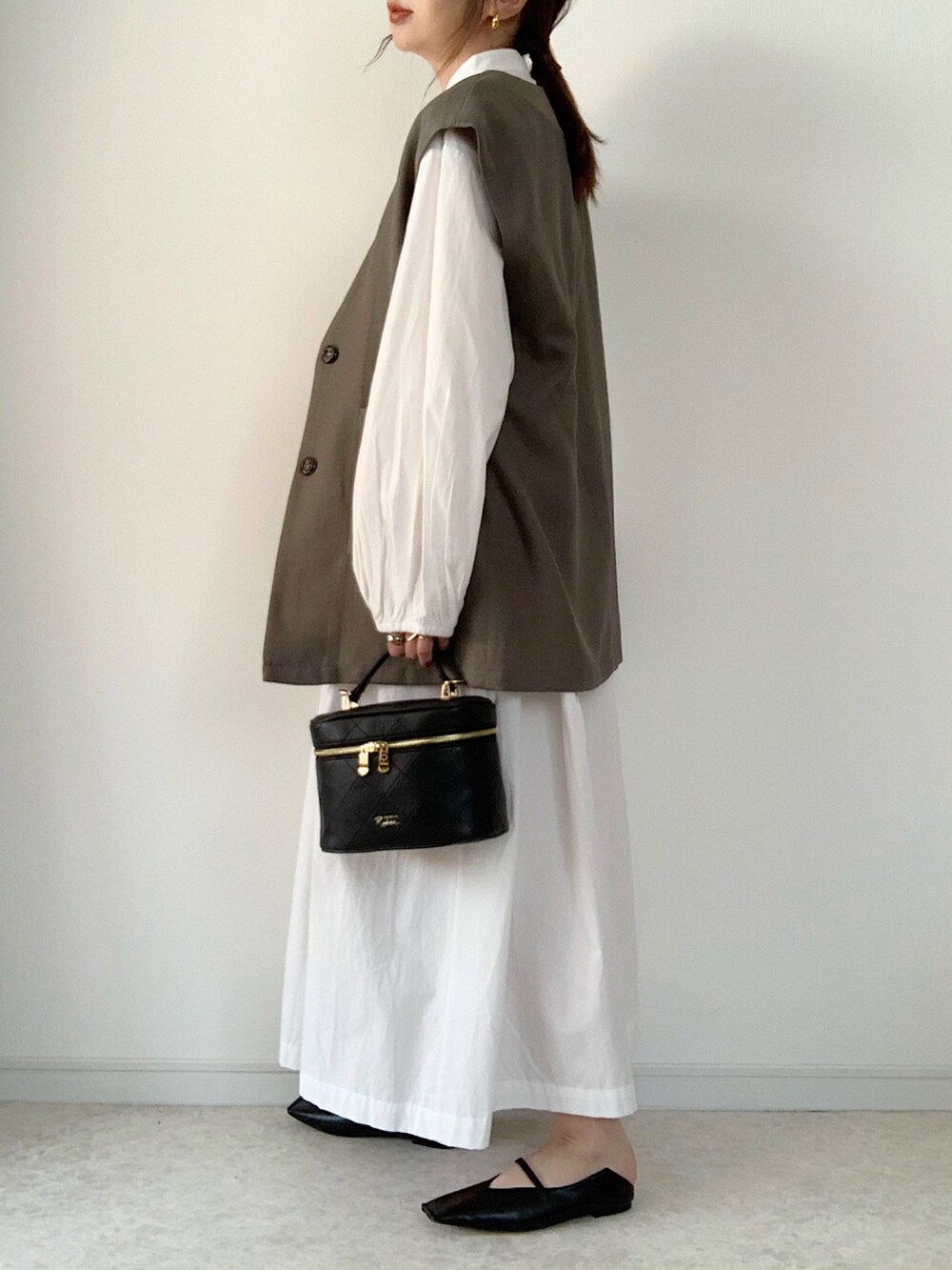 グレー系のベスト、ホワイト系のシャツワンピース、ブラック系のショルダーバッグを着用したレディースの春コーディネートの2枚目の写真