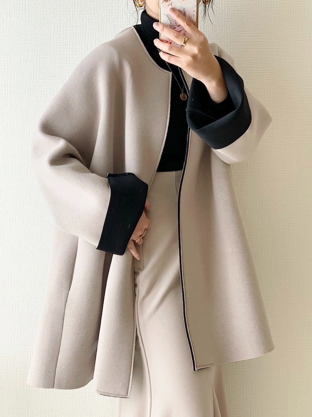 ベージュ系のノーカラーコート、ベージュ系のスカート、ホワイト系のブーツを着用したレディースの秋コーディネートの2枚目の写真