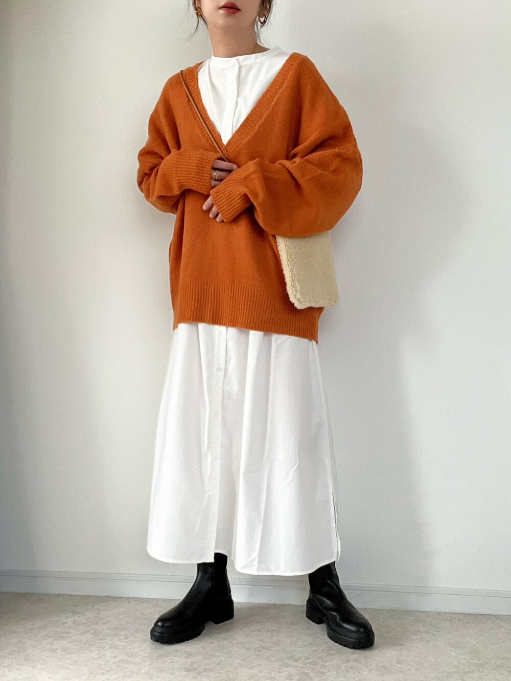オレンジ系のニット/セーター、ホワイト系のシャツワンピース、ブラック系のブーツを着用したレディースの秋コーディネートの2枚目の写真