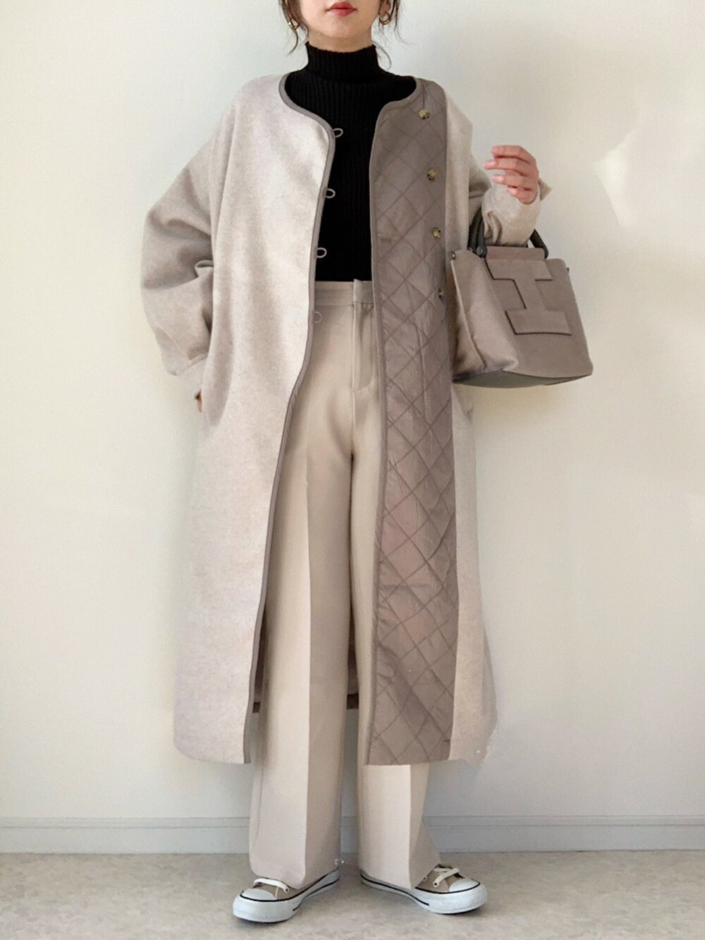 ベージュ系のノーカラーコート、ブラック系のハンドバッグ、ホワイト系のスニーカーを着用したレディースの冬コーディネートの2枚目の写真