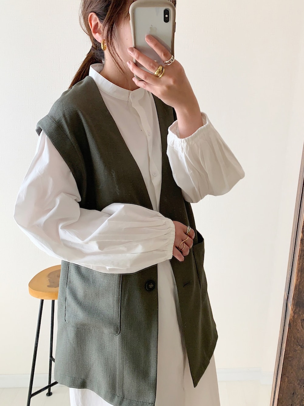 グレー系のベスト、ホワイト系のシャツワンピース、ブラック系のショルダーバッグを着用したレディースの春コーディネートの3枚目の写真