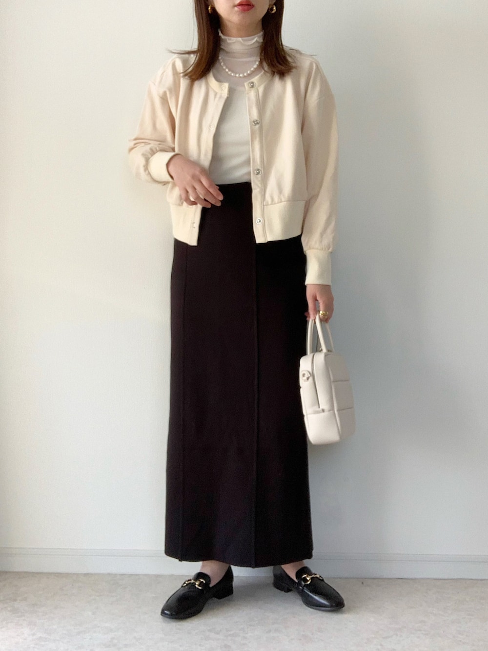ホワイト系のカーディガン/ボレロ、ブラック系のスカート、ブラック系のローファーを着用したレディースの春コーディネートの2枚目の写真