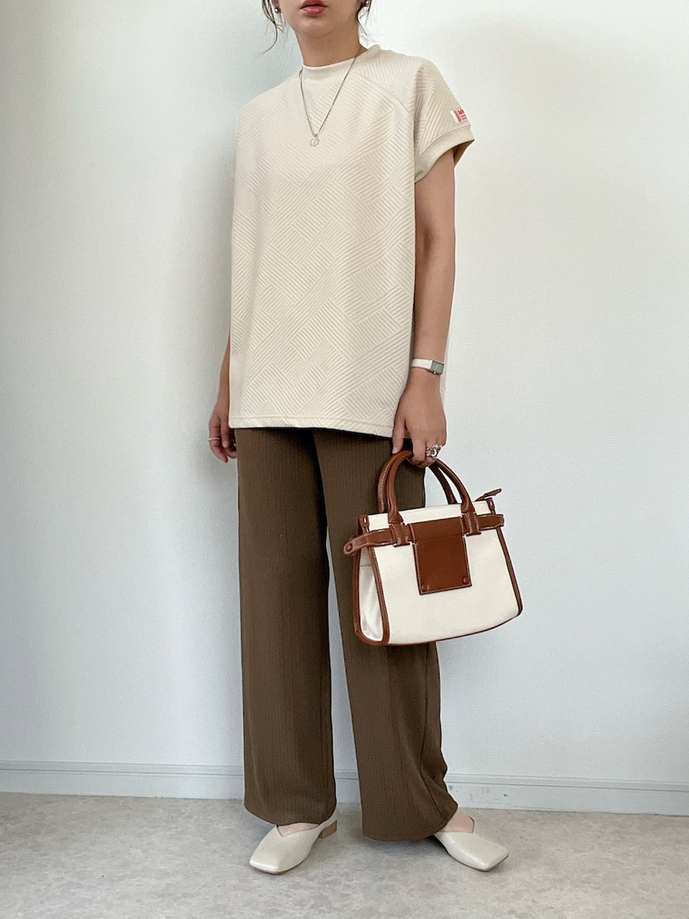 ベージュ系のTシャツ/カットソー、ベージュ系のスラックス、ブラウン系のハンドバッグを着用したレディースの夏コーディネートの2枚目の写真