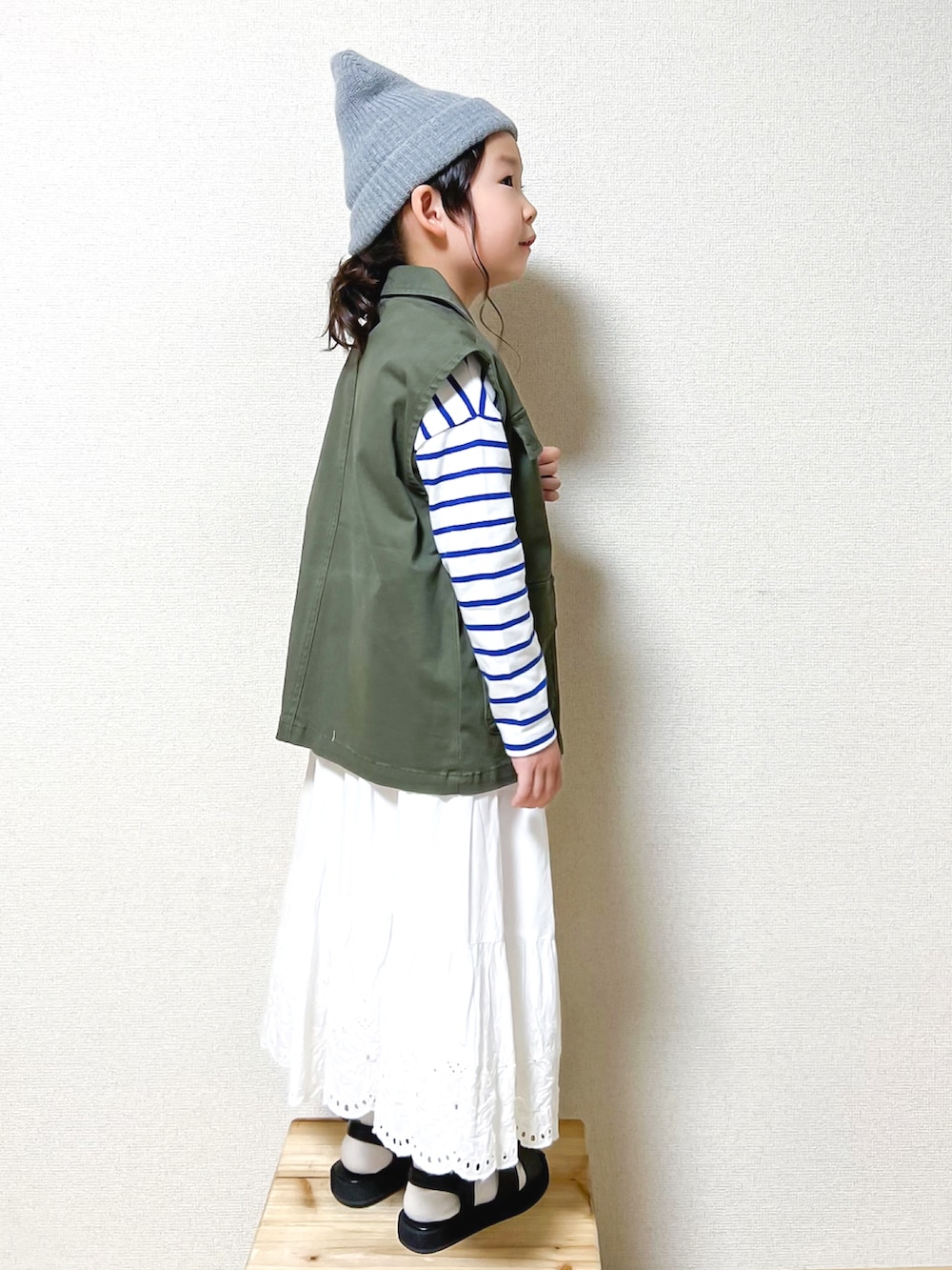 グリーン系のベスト、ホワイト系のTシャツ/カットソー、ホワイト系のスカートを着用したキッズの秋コーディネートの2枚目の写真