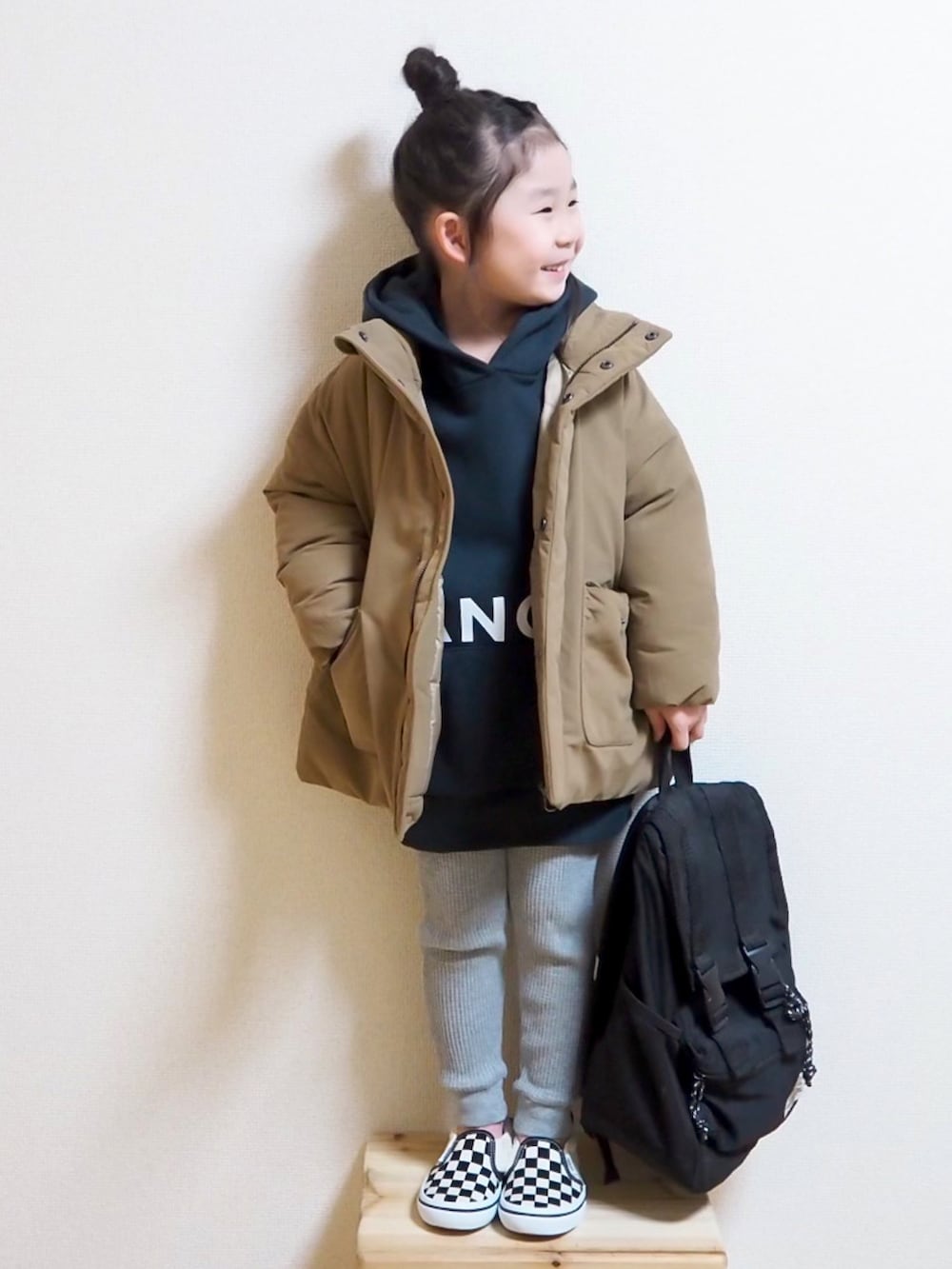 ベージュ系のダウンジャケット/コート、ブラック系のパーカー、ブラック系のスリッポンを着用したキッズの冬コーディネートの2枚目の写真