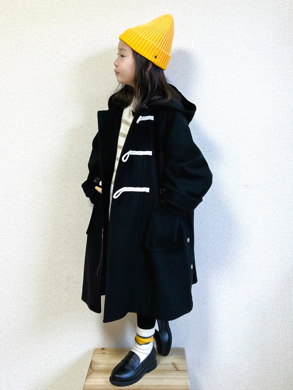 ブラック系のダッフルコート、ホワイト系のニット/セーター、ブルー系のデニムパンツを着用したキッズの秋コーディネートの2枚目の写真