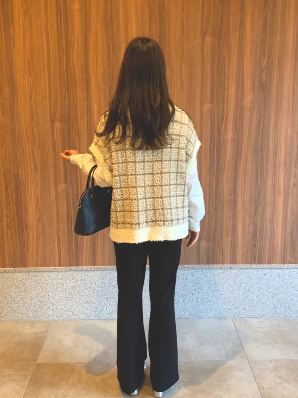 ブルー系のバッグ、ホワイト系のベスト、ブラック系のスラックスを着用したレディースの秋コーディネートの2枚目の写真