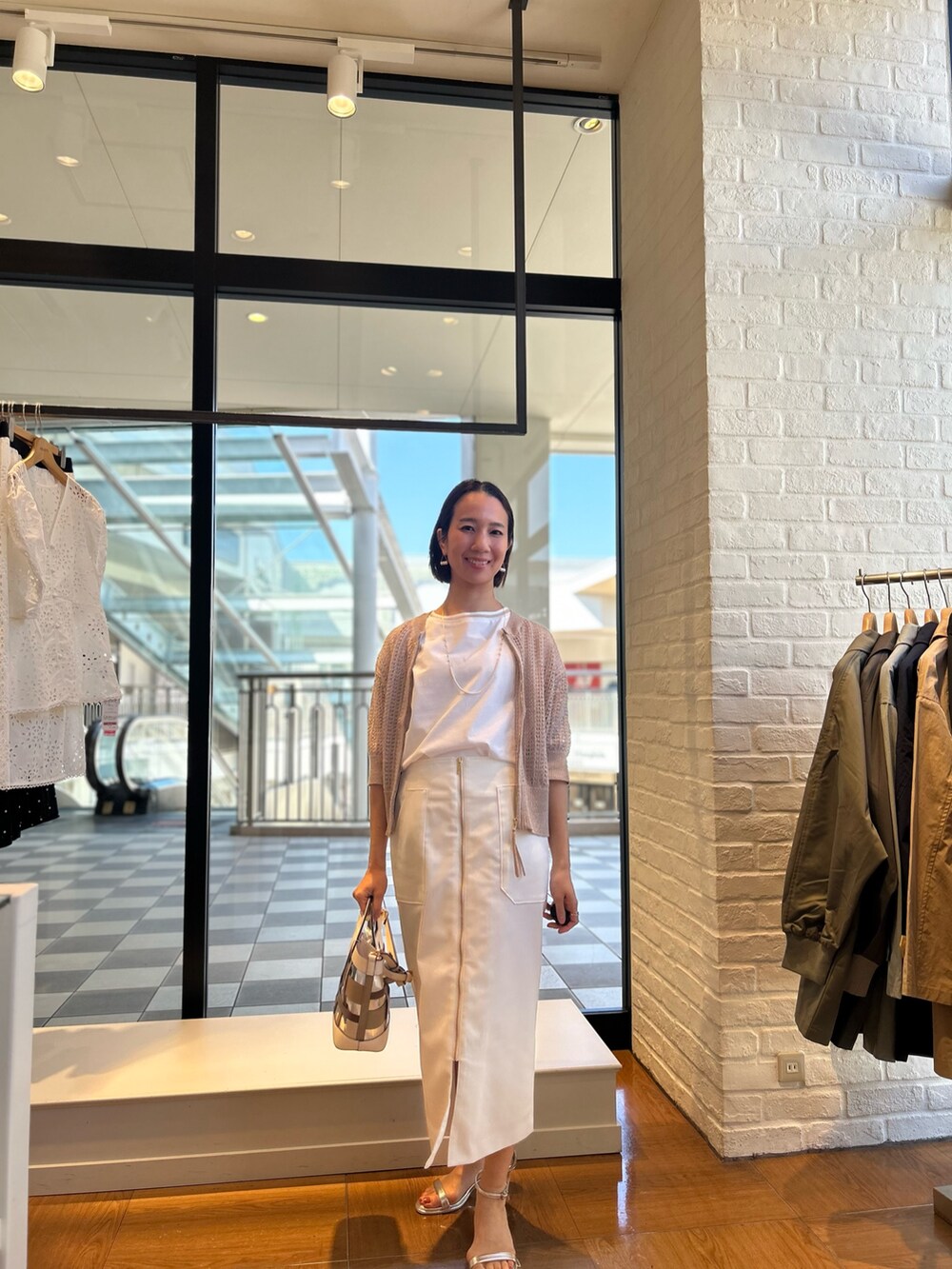 ホワイト系のスカート、ホワイト系のTシャツ/カットソー、ベージュ系のニット/セーターを着用したレディースの春コーディネートの2枚目の写真