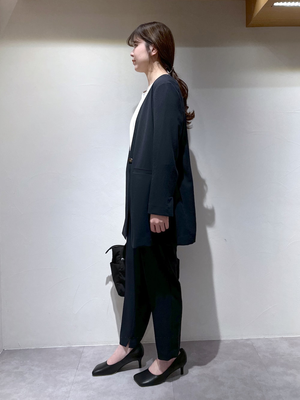 ブラック系のトートバッグ、ブルー系のスラックス、ブルー系のノーカラージャケットを着用したレディースの春コーディネートの3枚目の写真